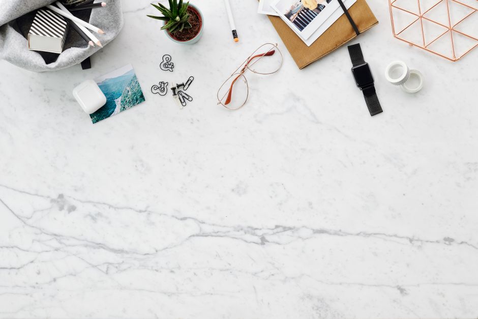Plan de travail en marbre avec accessoires de bureau, plantes, lunettes et carnet, idéal pour cuisiner sereinement.