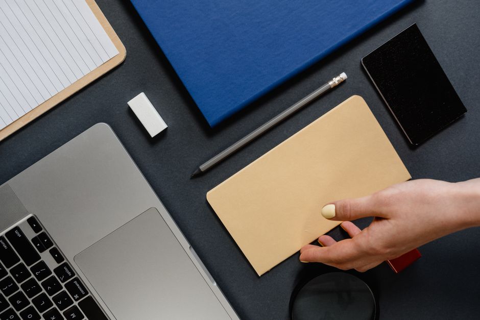 Plan de travail organisé avec un ordinateur portable, des carnets, un stylo et une main tenant une enveloppe.